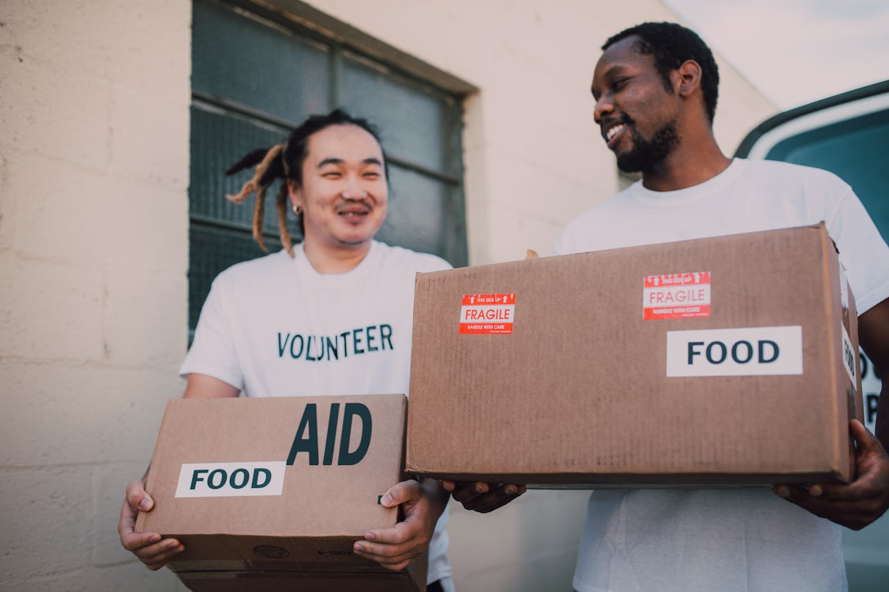 Two volunteers carrying aid boxes labeled food, showing community support and charity efforts.